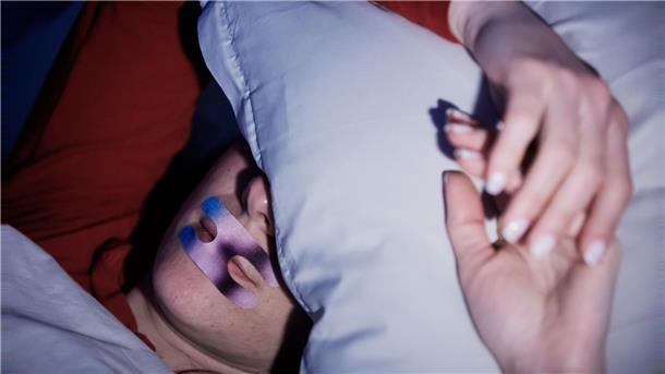 Eine Frau liegt mit einem Mundpflaster im Bett. Ob es hilft? (Illustration)