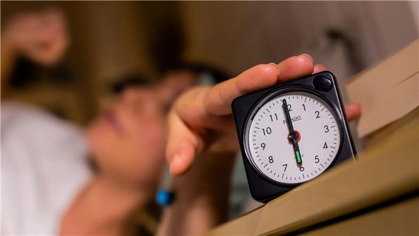 Eine Frau schaltet vom Bett aus einen auf sechs Uhr gestellten Wecker aus. 