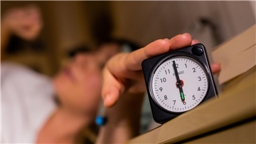 Eine Frau schaltet vom Bett aus einen auf sechs Uhr gestellten Wecker aus. 