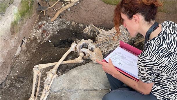 Eine Frau sitzt vor einem Skelett im Archäologiepark Pompeji.