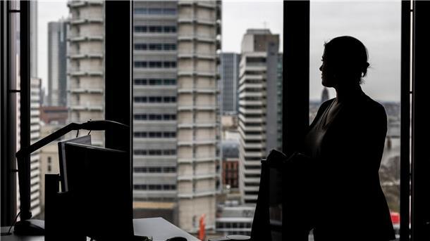 Studie: Wenige Frauen in Führungspositionen Eine Frau steht an ihrem Arbeitsplatz in einem Hochhaus am Fenster.