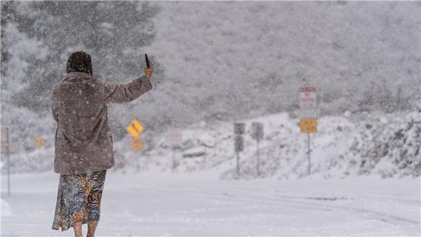 Eine Frau steht auf einer schneebedeckten Straße und macht ein Selfie im Angeles National Forest.