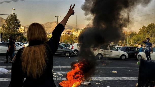 Eine Frau steht im September 2022 während einer Demonstration nach dem Tod der 22-jährigen Mahsa Amini vor einem brennenden Autoreifen und zeigt das Victory-Zeichen.