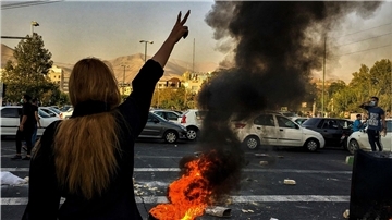 Eine Frau steht im September 2022 während einer Demonstration nach dem Tod der 22-jährigen Mahsa Amini vor einem brennenden Autoreifen und zeigt das Victory-Zeichen.