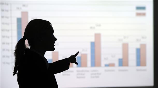 Studie: Vorstandsfrauen verdienen im Schnitt mehr als Männer Eine Frau steht in einem Büro und erklärt eine an die Wand projezierte Grafik.