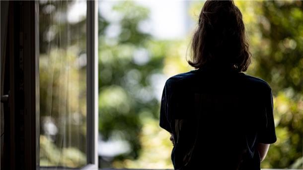 Eine Frau steht in ihrer Wohnung an einem Fenster. Im Land Bremen soll die Isolationspflicht bei Corona-Infizierten vorerst bestehen bleiben.