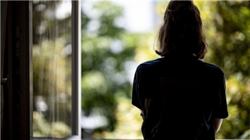 Eine Frau steht in ihrer Wohnung an einem Fenster. Im Land Bremen soll die Isolationspflicht bei Corona-Infizierten vorerst bestehen bleiben.