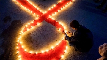 Eine Frau stellt Kerzen auf, die eine rote Schleife formen - ein weltweit anerkanntes Symbol für die Solidarität mit HIV-Infizierten.