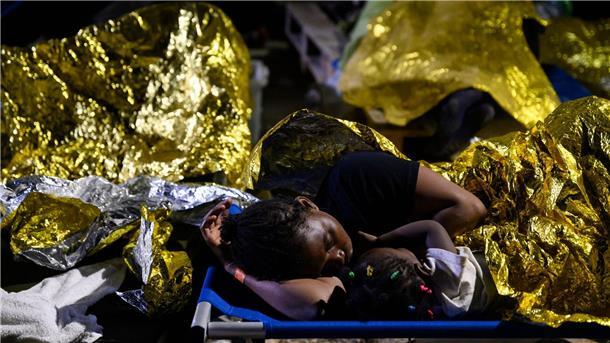 Eine Frau und ein Kind sowie weitere Menschen schlafen im Freien vor dem Erstaufnahmelager auf Lampedusa.