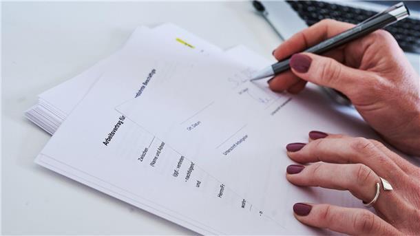 Eine Frauenhand unterschreibt einen Arbeitsvertrag.