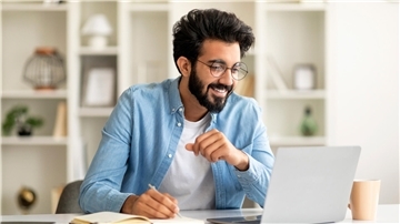 Ein junger dunkelhaariger Mann sitzt am Schreibtisch und arbeitet am Laptop.