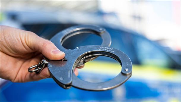 Drei Festnahmen wegen Brandstiftung und versuchten Mordes Eine Hand hält Handschellen vor einen Streifenwagen der Polizei.