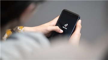 Eine Jugendliche schaut auf ein Smartphone mit angezeigtem TikTok Logo.