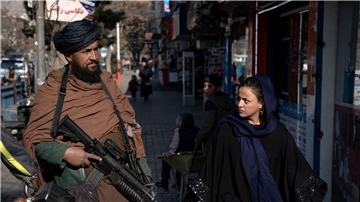 Eine junge Frau läuft in Kabul an einem Taliban-Kämpfer vorbei.