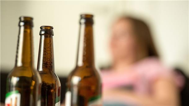 Digitale Suchtberatungsplattform bereit Eine junge Frau sitzt hinter leeren Bierflaschen.