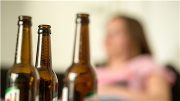 Eine junge Frau sitzt hinter leeren Bierflaschen.