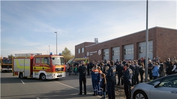Menschen stehen vor einem Großen Gebäude, davor stehen Feuerwehrautos. 