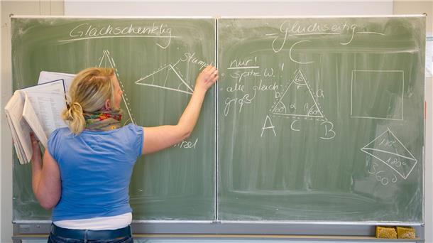 Eine Lehrerin schreibt mit Kreide an die Tafel.