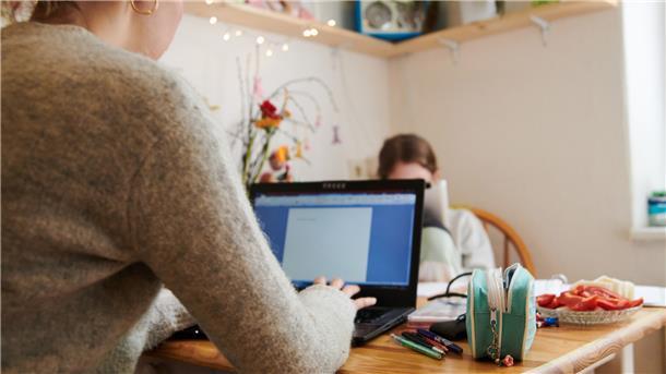 Eine Mutter arbeitet am Küchentisch, während ihre Tochter gegenüber in ein Tablet guckt. Nach Ansicht von Experten sollten Unternehmen darauf achten, dass nicht vor allem Frauen im Homeoffice arbeiten, während Männer im Büro bleiben.
