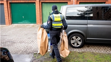 Eine Polizistin trägt Beweismittel aus einem Mehrfamilienhaus. Eine Hundertjährige soll dort von ihrem Enkel getötet worden sein.