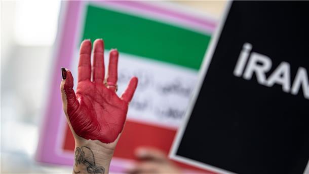 Eine rot bemalte Hand einer Demonstrantin erhebt sich zwischen Plakaten während einer Demonstration vor dem iranischen Konsulat in Istanbul.