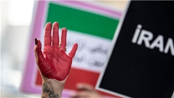 Eine rot bemalte Hand einer Demonstrantin erhebt sich zwischen Plakaten während einer Demonstration vor dem iranischen Konsulat in Istanbul.
