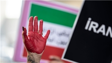 Eine rot bemalte Hand einer Frau erhebt sich zwischen Plakaten während einer Demonstration.