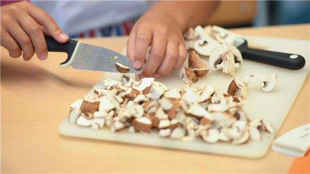 Eine Schülerin schneidet während der Koch AG Champignons in kleine Scheiben.