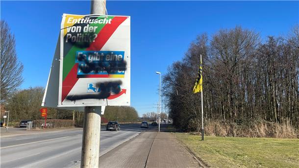 Beschmiertes Wahlplakat an einer Straße.