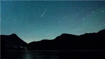 Eine Sternschnuppe leuchtet neben der Milchstraße am Himmel über dem Walchensee.