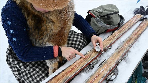 Historisches Rennen „Nostalski“ mit Ski aus Holz Eine Teilnehmerin wachst ihre Holzskier mit einer Kerze.
