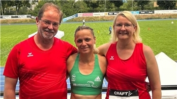 Drei Leichtathleten stehen auf der Tribüne eines Stadions.
