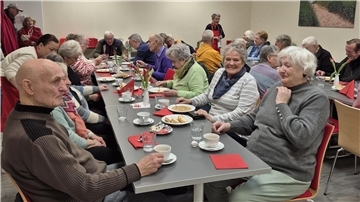 Viele Menschen sitzen an Tischen und essen Suppe. 