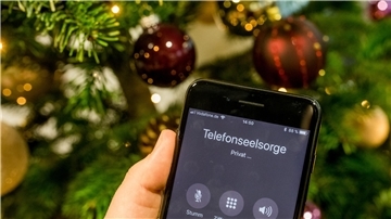 Auf dem Display eines Handys wird ein Anruf bei der Telefonseelsorge gezeigt. Im Hintergrund ist ein Weihnachtsbaum zu sehen.