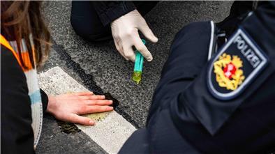 Einsatzkräfte der Polizei lösen den Klebstoff, mit dem sich eine Aktivistin festgeklebt hat.