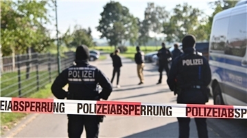Einsatzkräfte der Polizei stehen hinter einer Polizeiabsperrung nach einer Razzia in Hesselbronn.