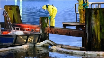Einsatzkräfte des THW in Schutzanzügen arbeiten mit Ölschlengeln an einem Steg. Aus einem Leck in einer Pipeline im Hafen von Brunsbüttel sind große Mengen Öl in den Nord-Ostsee-Kanal gelaufen.