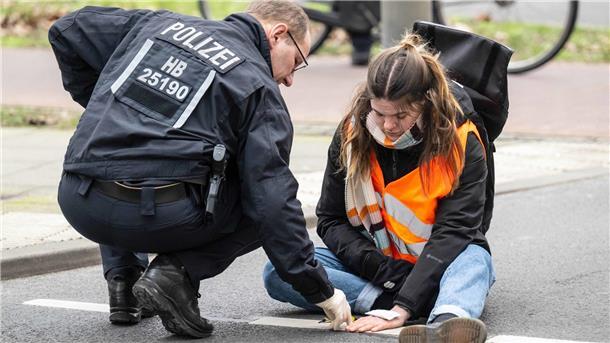 Einsatzkräfte lösen den Klebstoff, mit dem sich eine Aktivistin der Letzten Generation an der Straße festgeklebt hat. Die Klimaaktivisten blockieren so immer wieder den Verkehr. 