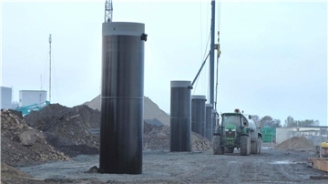Baustelle im neuen BLG-Südhafen „Roter Sand“ in Bremerhaven: Mehrere massive schwarze Hochpoller stehen in einer Reihe, im Hintergrund sind Baumaschinen, Erdhaufen und ein Traktor mit Anhänger zu sehen.
