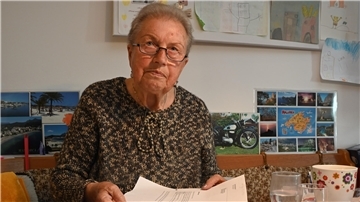 Eine Frau mit Brille. Sie sitzt an einem Tisch und zeigt die Zettel in die Kamera.