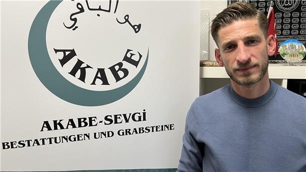 Enes Sevgi neben dem Logo seines Bestattungsunternehmens. 