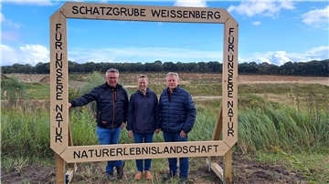 Bürgermeister Andreas Wittenberg (l.), Karla Mombeck von der BI MUT und Ortsbürgermeister Heinz Bühring weihen den neuen Fotorahmen an der Schatzgrube Weißenberg ein. 