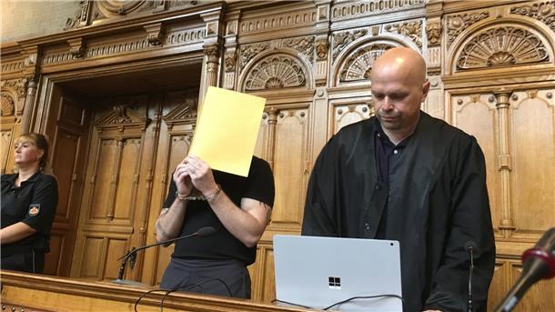 Zwei Männer, einer hält eine Mappe vor das Gesicht