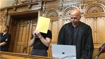 Zwei Männer, einer hält eine Mappe vor das Gesicht