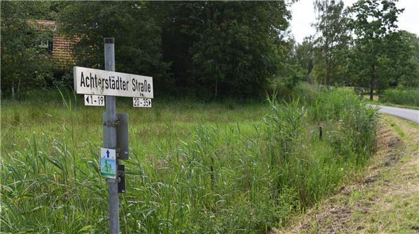 Straßenschild auf dem Achterstädter Straße zu lesen ist, viel grün und rechts ein bisschen Straße