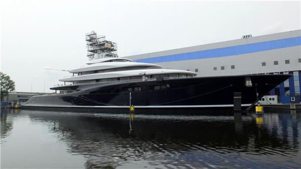 Megayacht mit schwarzem Rumpf vor einer Schiffsbauhalle