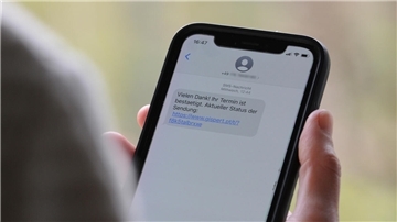 Ein Handy, auf dem eine SMS zu sehen ist. Das Handy wird in der Hand gehalten. Die Person ist nicht im Bild.