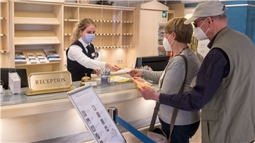 Ein Ehepaar zeigt an der Rezeption eines Hotels die Impfausweise vor. 