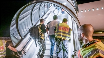 Männer führen einen Mann die Treppe zum Flugzeug hinauf