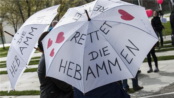 Zwei Frauen tragen am 12.04.2014 in Berlin bei einem Protestumzug für den Erhalt der freien Geburtenhilfe Regenschirme mit der Aufschrift "Rettet die Hebammen".